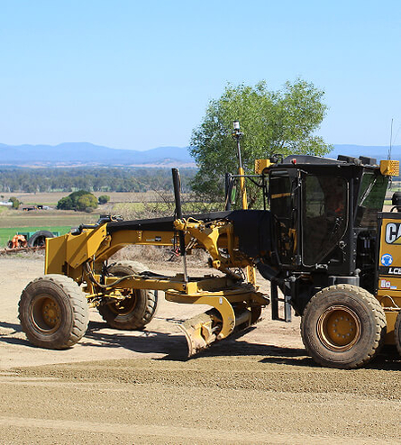 Road construction with machinery in focus and mountains in the distant background